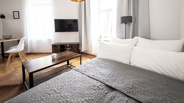 A modern living room with a sofa, a coffee table, a TV, and a dining area with a chair and table. - FirstClass 2-room apartment (Leipzig)