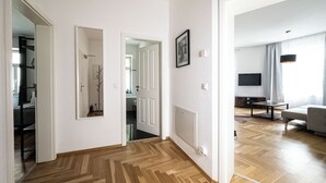 A hallway with wooden flooring, white walls, and a door leading to a living area with a sofa and a TV. - FirstClass 2-room apartment (Leipzig)
