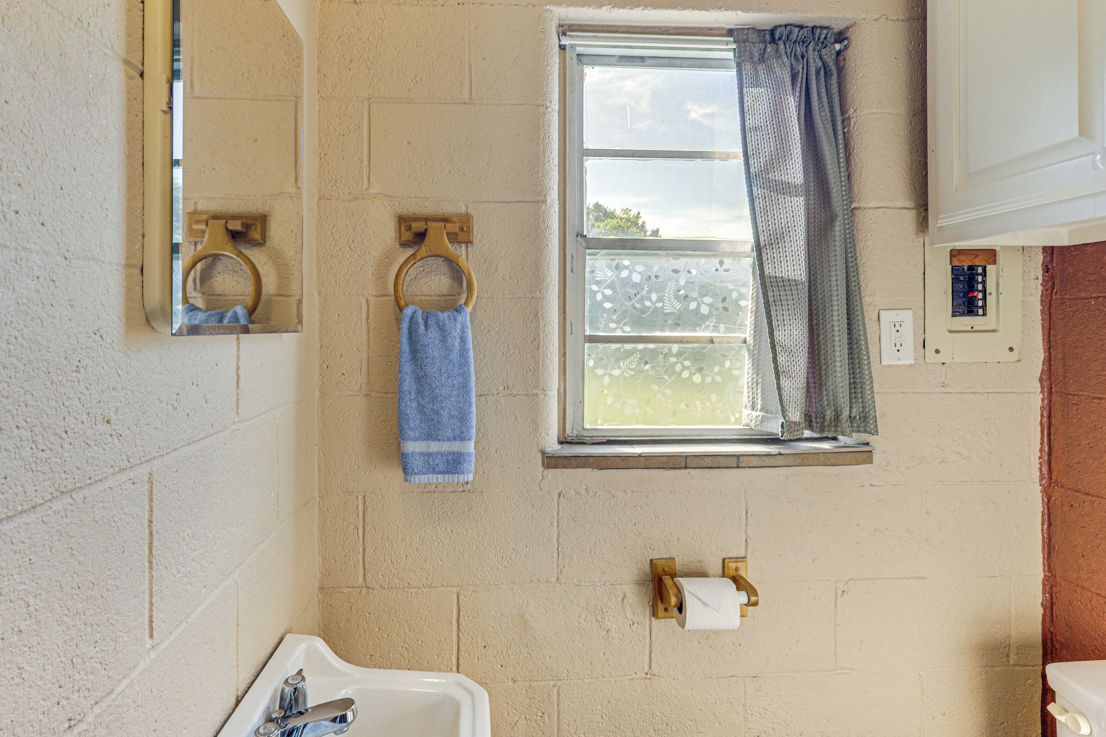 A bathroom with a sink, mirror, towel rack, window with curtains, and a toilet.