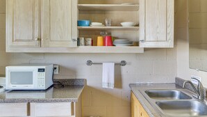 Una cocina con armarios de madera, un microondas, un fregadero y varios platos y tazas en las estanterías.