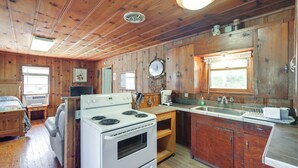 A cabin-style kitchen with wooden walls, a stove, a sink, and a dining area with a table and chairs. - On-Site Trails! Cozy Whitney Cottage 2 Mi to Lake (Whitney)