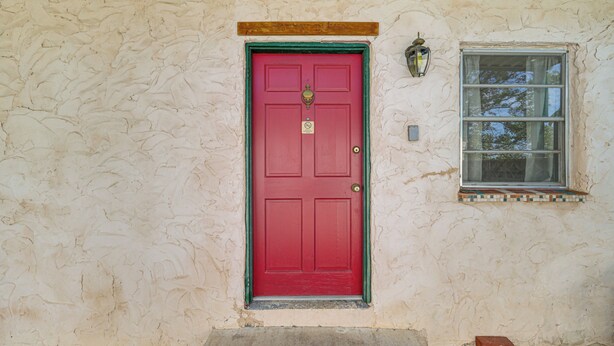 A red door with a green frame, a small window with a tiled ledge, and a yellow line on the ground. - Patio & Trail Access: Lake Whitney Studio! (Whitney)