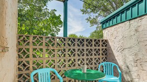 A patio area with a green table and two blue chairs, a decorative lattice fence, and a white wall with textured surface. - Patio & Trail Access: Lake Whitney Studio! (Whitney)
