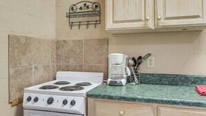 A kitchen with a white stove, a coffee maker, and wooden cabinets. - Patio & Trail Access: Lake Whitney Studio! (Whitney)
