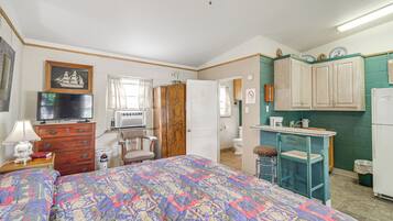 A bedroom with a bed, dresser, TV, and a small kitchenette with a fridge, stove, and sink.