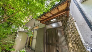 A traditional Japanese-style building with a wooden entrance, a sliding door, and a small garden area with plants and a bench.