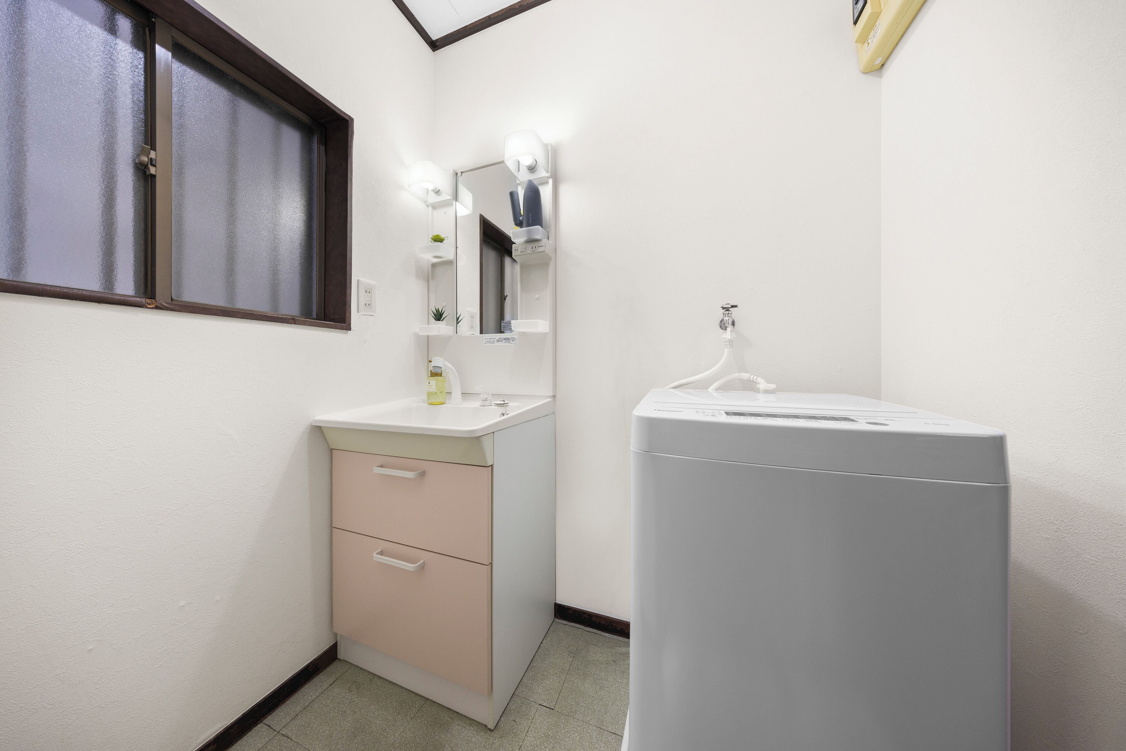 A small, clean bathroom with a sink, mirror, and a washing machine.