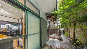 A modern interior with a sliding glass door leading to a dining area, a small outdoor garden area with a wooden bench, and a potted plant.