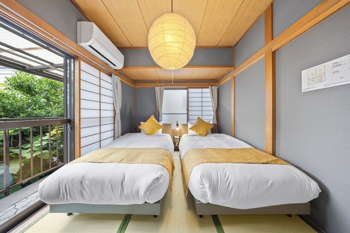 A room with two beds, a wooden ceiling, and a large window.