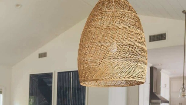 Una sala moderna con una mesa redonda de madera, una lámpara colgante tejida, un sofá gris con cojines y una silla gris de fibra.
