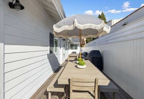 A wooden deck with a table and chairs, a striped umbrella, and a grill.