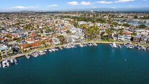 Vista aérea de un pueblo costero con edificios residenciales, un puerto deportivo con barcos y un cielo azul despejado.