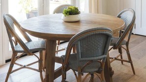 Comedor con una mesa redonda de madera, sillas de mimbre y una lámpara colgante tejida.