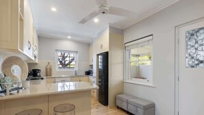 A modern kitchen with a central island, a built-in oven, and a refrigerator. There is a window providing natural light and a bench near the door.