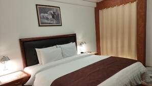 Ein Hotelzimmer mit einem großen Bett, einem Nachttisch mit Lampe, einem gerahmten Bild an der Wand und einem Fenster mit Vorhängen.