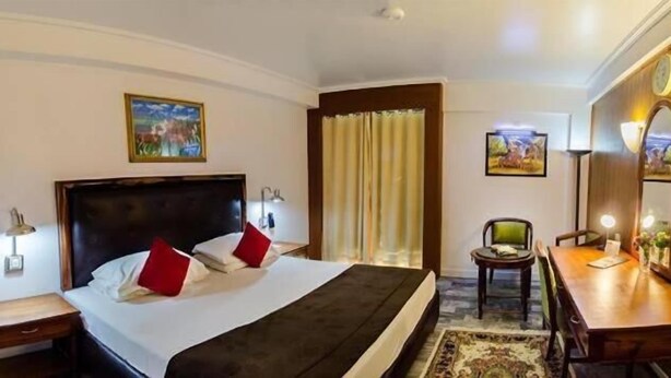 Ein Hotelzimmer mit einem großen Bett, einem Schreibtisch, einem Stuhl, einem Fernseher und Bildern an den Wänden.