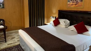 Ein Hotelzimmer mit einem großen Bett, Holzwandverkleidung, einem Gemälde, einem Nachttisch und einem Sessel.