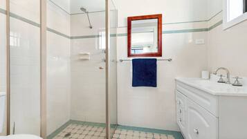 A bathroom with a glass shower enclosure, a white sink with a mirror above it, and a blue towel hanging on the wall.