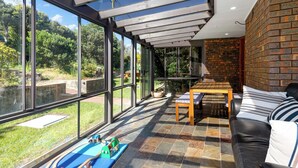 Un salon moderne doté de grandes fenêtres, d’un sol carrelé en pierre, d’une table en bois et d’un canapé en cuir noir.