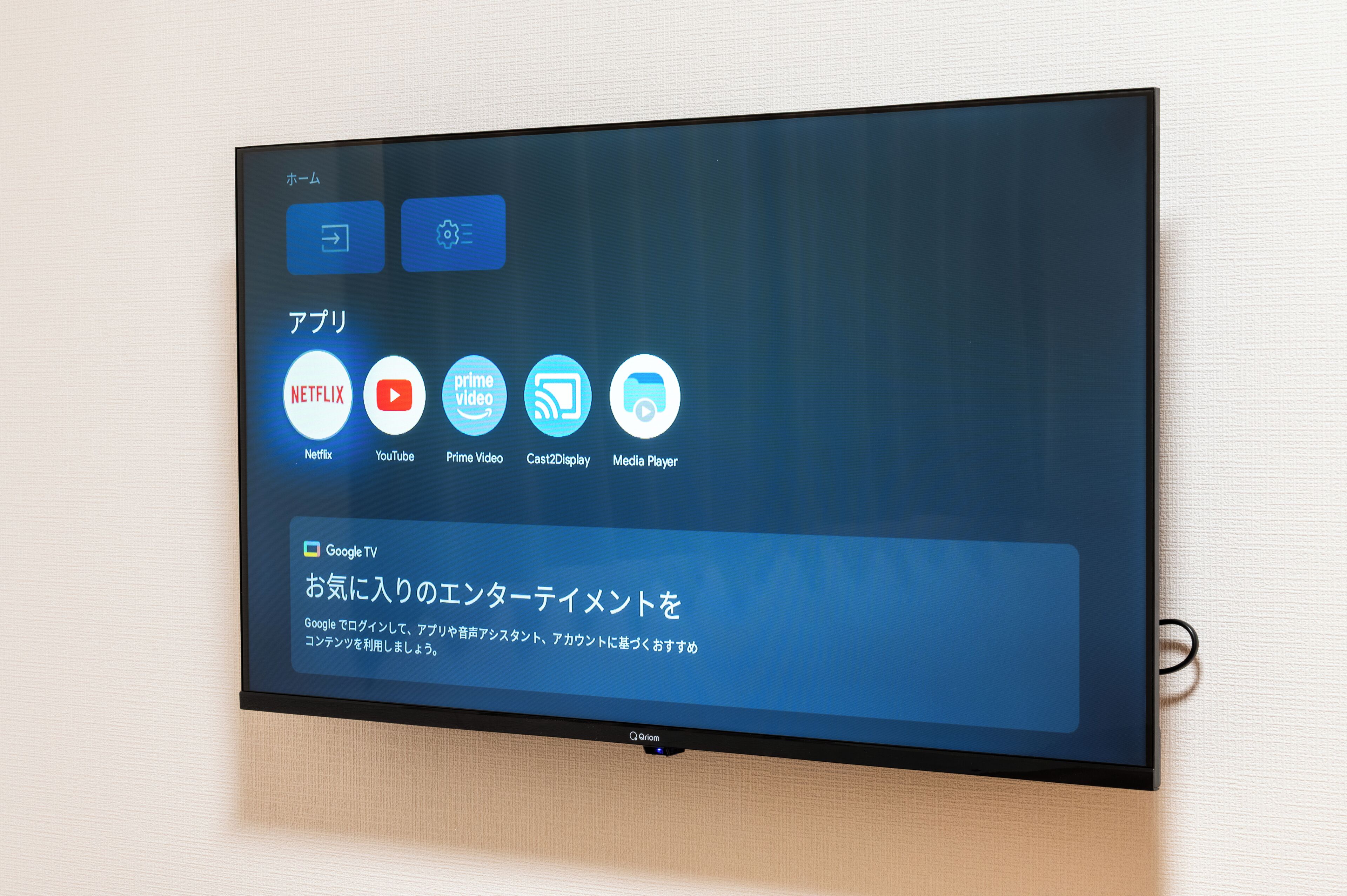 A flat-screen TV mounted on a wall displaying a media application interface with icons for Netflix, YouTube, Prime Video, Cast2Display, and Media Player.