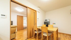 Une pièce comprenant une table à manger en bois, quatre chaises, un canapé et une porte coulissante donnant sur une autre pièce.