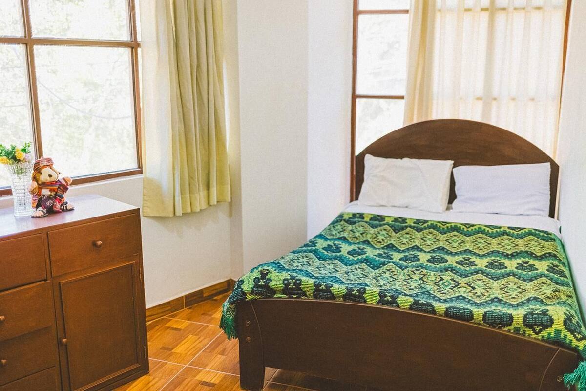 A bedroom with a wooden bed, a nightstand, and a window with curtains.