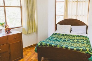 A bedroom with a wooden bed, a nightstand, and a window with curtains. - Hostal Aylluq Wasin  (Urubamba)