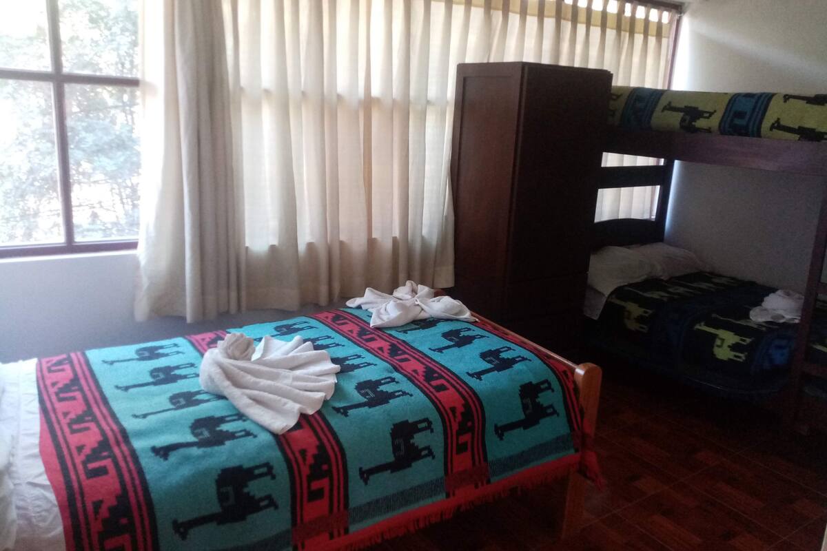 A room with a bed, a bunk bed, a window with curtains, and a wooden wardrobe.
