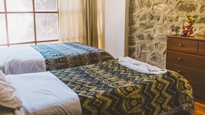 Una habitación con dos camas, una pared de piedra y un aparador con un oso de peluche.