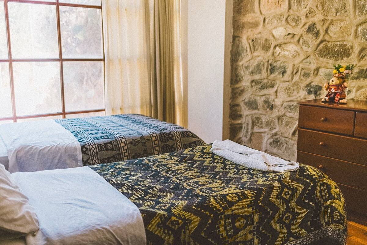 A room with two beds, a stone wall, and a dresser with a teddy bear.