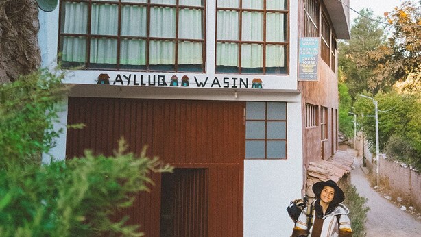 Un edificio de dos pisos con un letrero que dice "AYLLUQ WASIN" y un letrero que indica habitaciones de huéspedes.