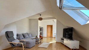 Un salon moderne avec un canapé gris, une chaise en bois, un meuble pour la télévision et une lucarne.