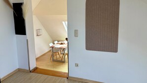 Une pièce avec un plancher en bois, une porte blanche ornée d’un panneau décoratif marron, un luminaire au plafond et une petite table avec des chaises.