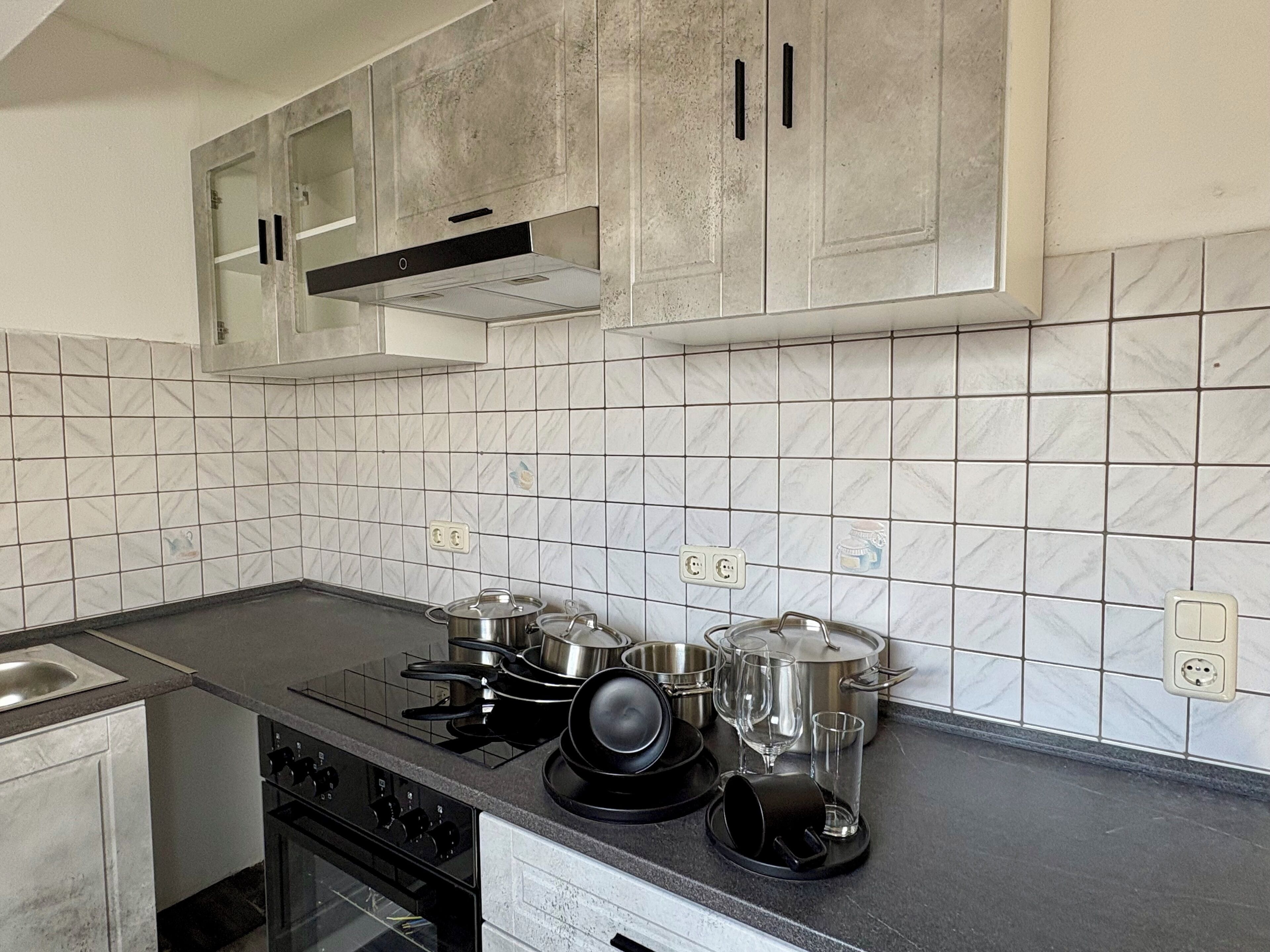 Una cocina con salpicadero de azulejos blancos, electrodomésticos de acero inoxidable y encimera negra.