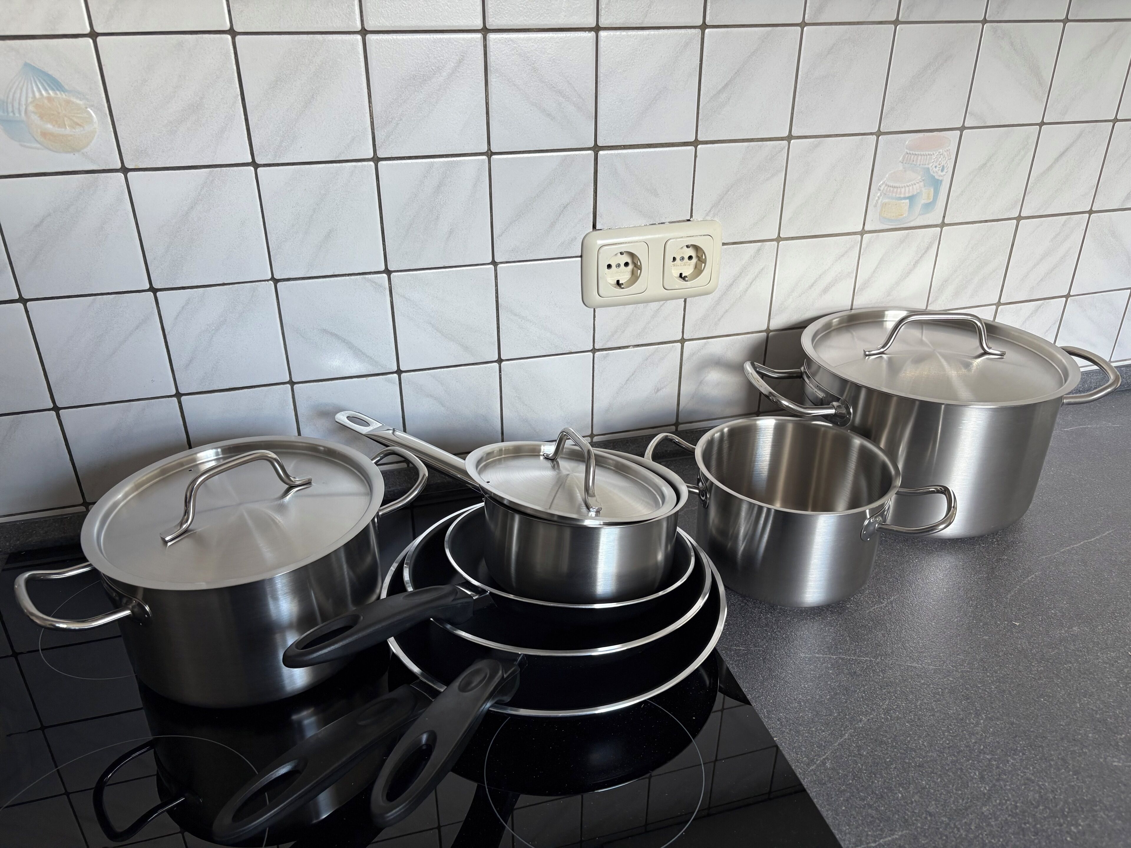 Keittiössä on neljä ruostumatonta teräskattilaa ja -pannua mustalla työtasolla, seinässä on kaksoispistorasia ja työtason yläpuolella on laatoitettu seinäpinta.