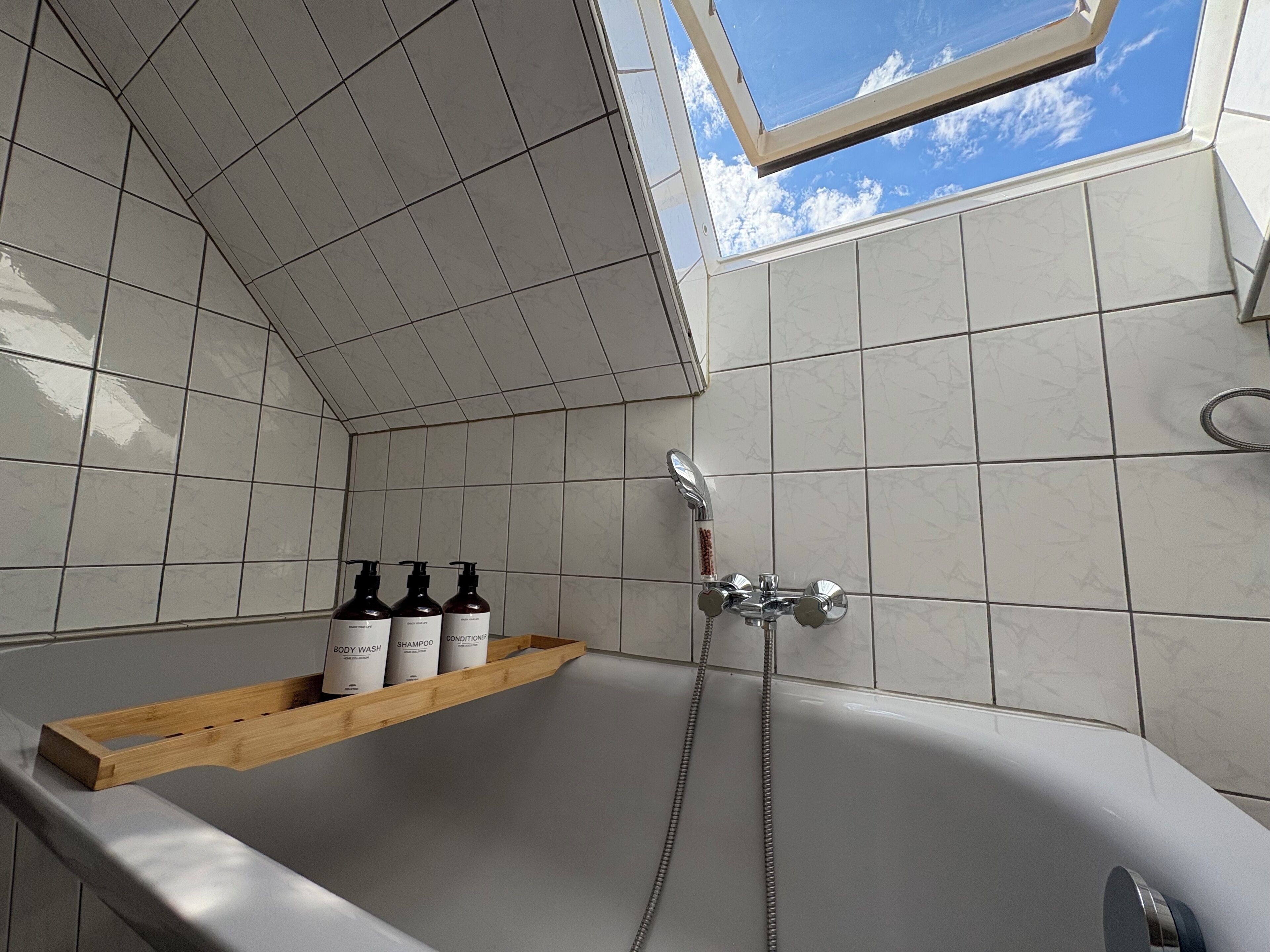 Un bagno con un lucernario, una doccia e uno scaffale con delle bottiglie.