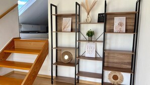 Un escalier en bois avec une rampe en bois et une étagère murale ornée d’objets décoratifs et d’une enseigne sur laquelle on peut lire « MAISON ».