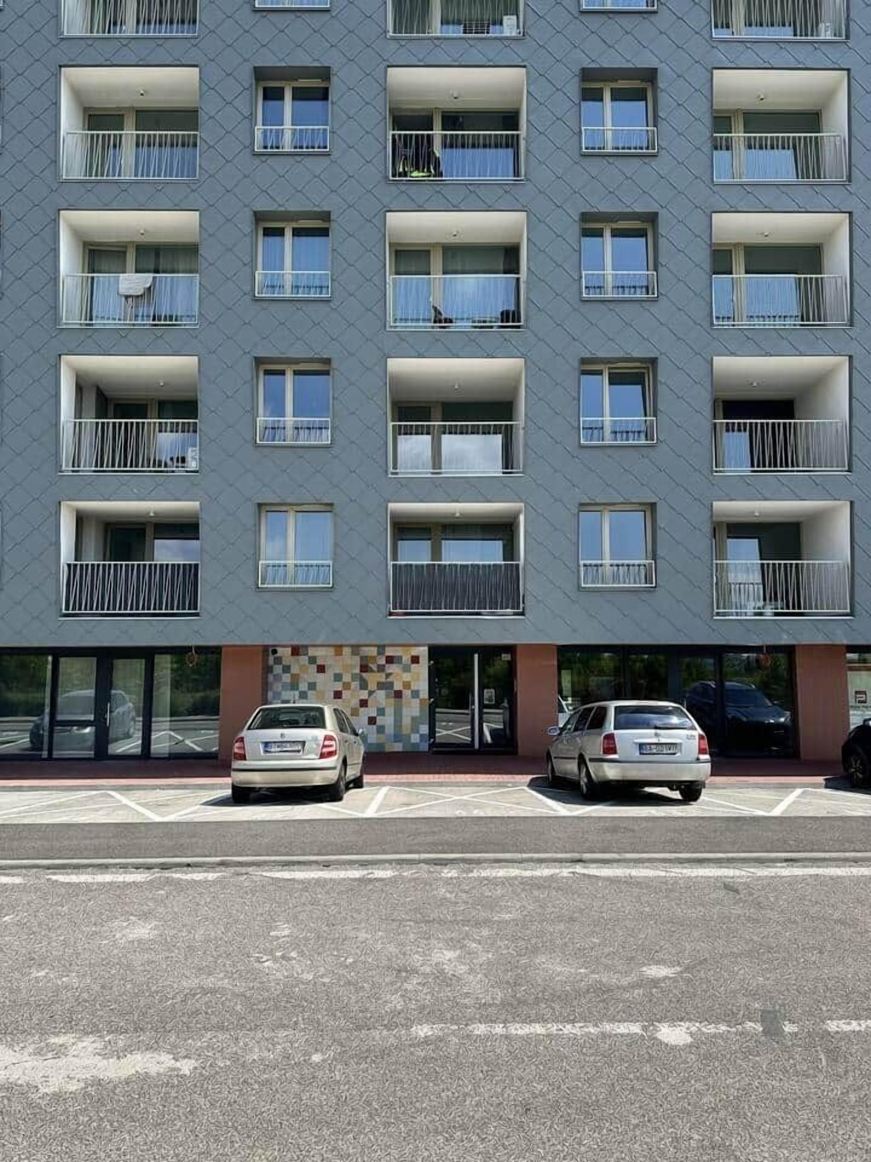 Ein mehrstöckiges Wohngebäude mit Balkonen, einem Parkplatz und einem Ladenlokal.