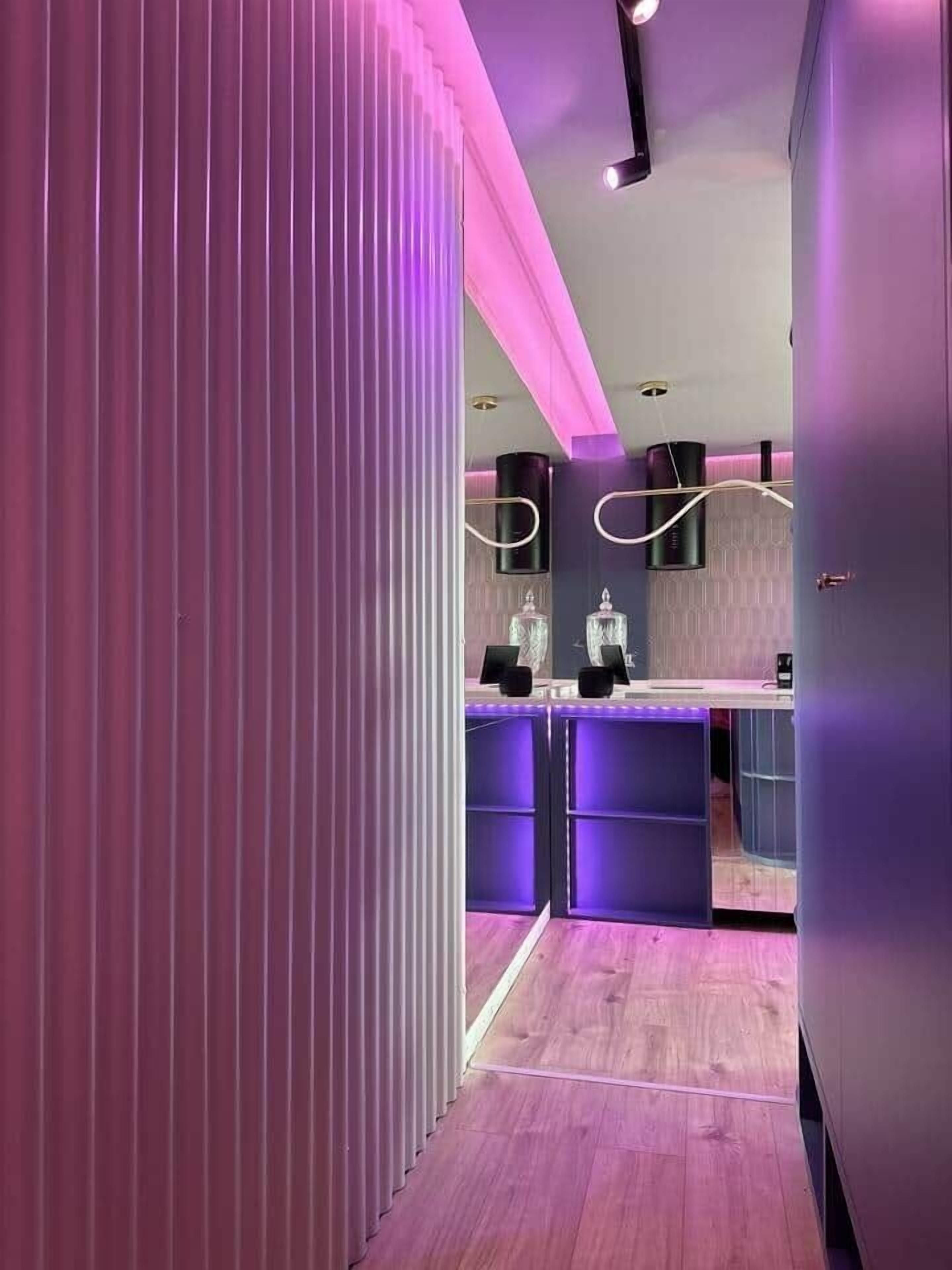 Un interior moderno con suelo de madera, una pared de acento rosa y una zona de bar con espejo y estanterías.