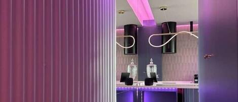 Un interior moderno con suelo de madera, una pared de acento rosa y una zona de bar con espejo y estanterías.
