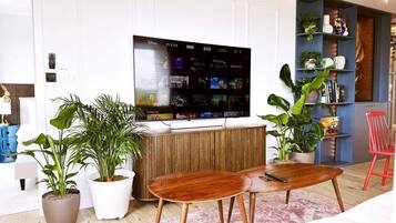 A modern living room with a flat-screen TV, wooden furniture, and potted plants.