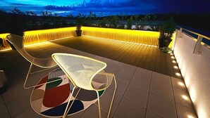 An outdoor patio with a table and chairs, a patterned rug, and a yellow-lit wall. - Ambient lounge with sundeck and free parking (Bratislava)