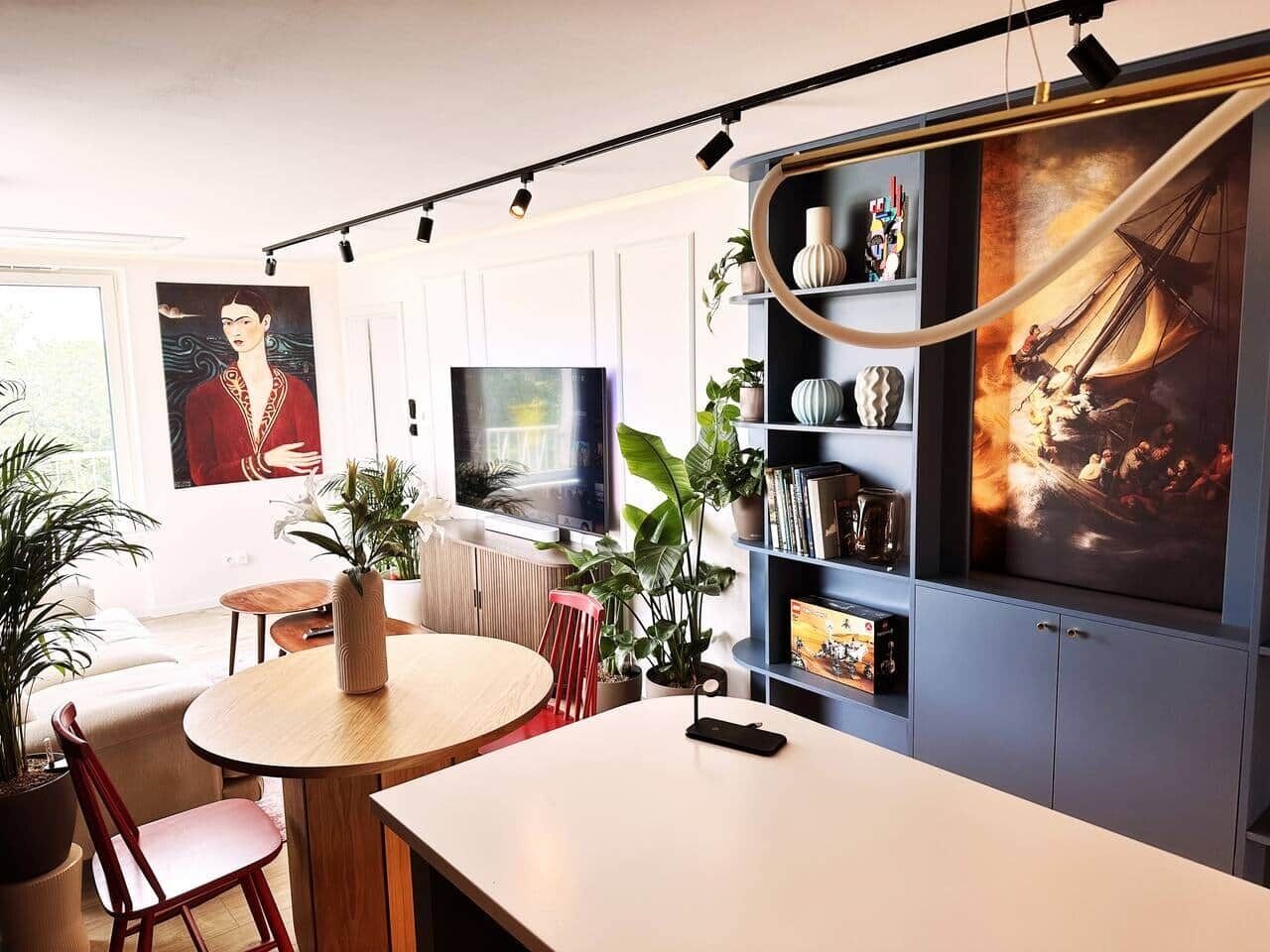 Un salon moderne avec une table à manger ronde, un téléviseur et une bibliothèque contenant divers objets.