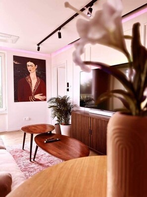 A modern living room with a large TV, a painting on the wall, a potted plant, and a wooden coffee table.