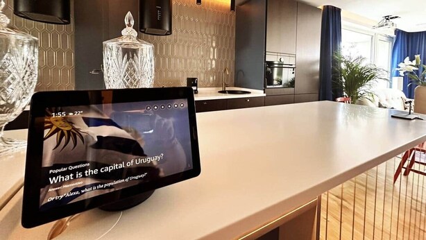A modern kitchen with a tablet displaying a video, a large island, and a view of the living area. - Ambient lounge with sundeck and free parking (Bratislava)