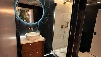 Ein modernes Badezimmer mit rundem Spiegel, Waschbecken in Weiß und einer Duschkabine aus Glas.