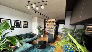Un salon moderne avec un canapé, une table basse et des plantes en pot. On y trouve également un coin cuisine avec des placards et un plan de travail.