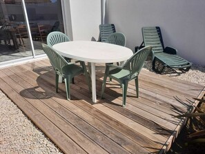 Um pátio com uma mesa redonda e seis cadeiras, ladeado por um deck de madeira e cascalho.