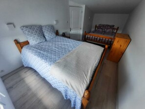 Quarto com uma cama grande, uma cama menor e uma cabeceira de madeira.