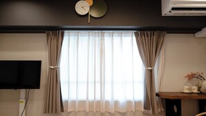 A room with a large window, curtains, a flat-screen TV, an air conditioner, and a small table with decorative items. - Shinjuku commercial area-Shinjuku Area-East Shinjuku Shinjuku-2Room-Max5P-Japanese style-Ueno Shinjuku-Ikebukuro-Shibuya Direct access (新宿区新宿)